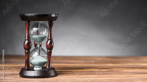 Transparent sand hourglass on wooden desk against gray background