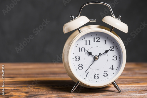 An old vintage alarm clock on wooden desk against black background