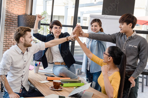 Group of five creative workers giving each other high-five with big smile on face, successful team performance, finishing touch photo