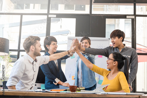 Group of five creative workers giving each other high-five with big smile on face, successful team performance, finishing touch photo