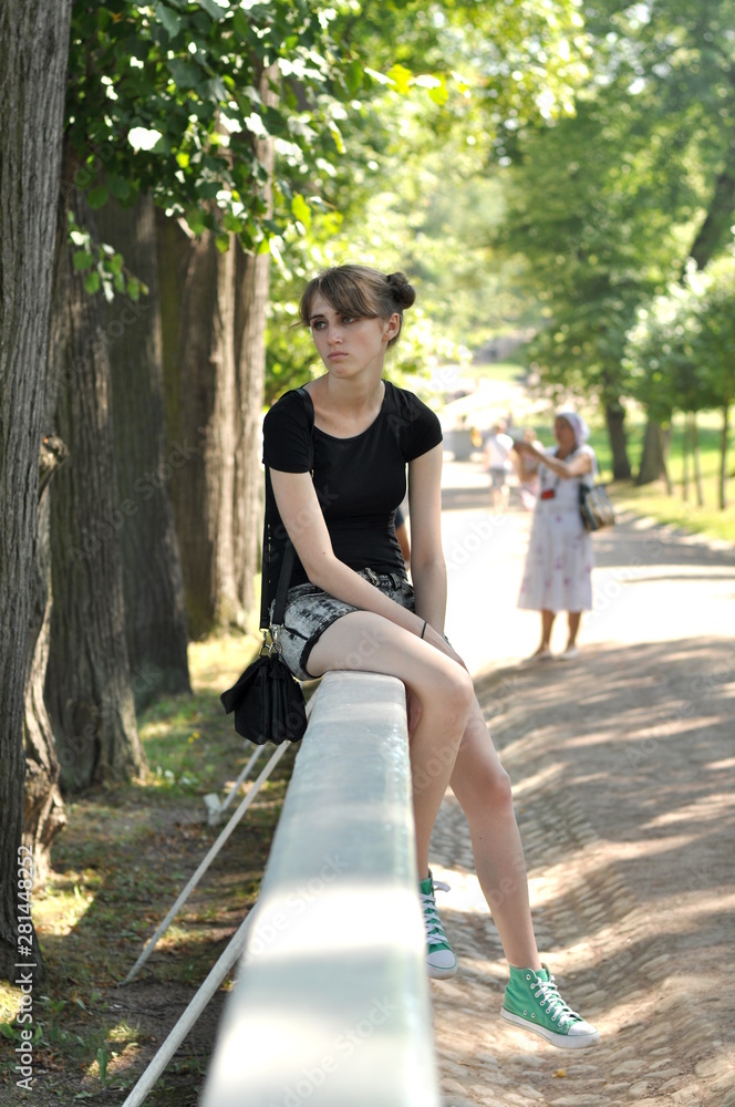 Sad blonde sits on the railing and looks into the distance. Bright, sunny day.