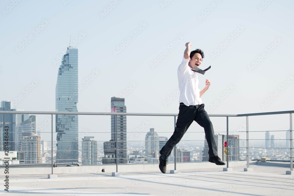 Happy businessman jumping after him work successful on top of building.