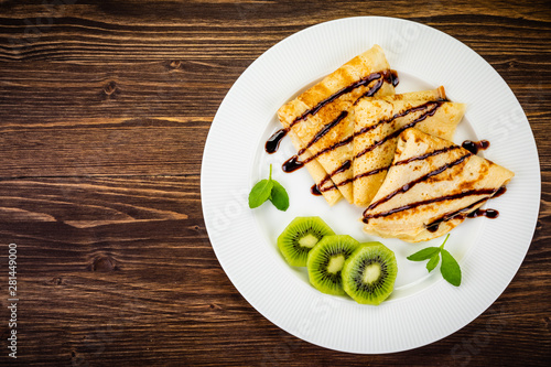 Crepes with kiwi and cream on wooden background