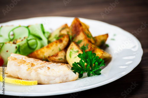 Fried fish with baked potatoes on wooden table