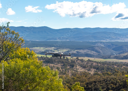 A small modern unmanned aerial vehicle drone in flight showing telegraph wires, landscape views and country scenery looking west of Canberra in the Australian Capital Territory