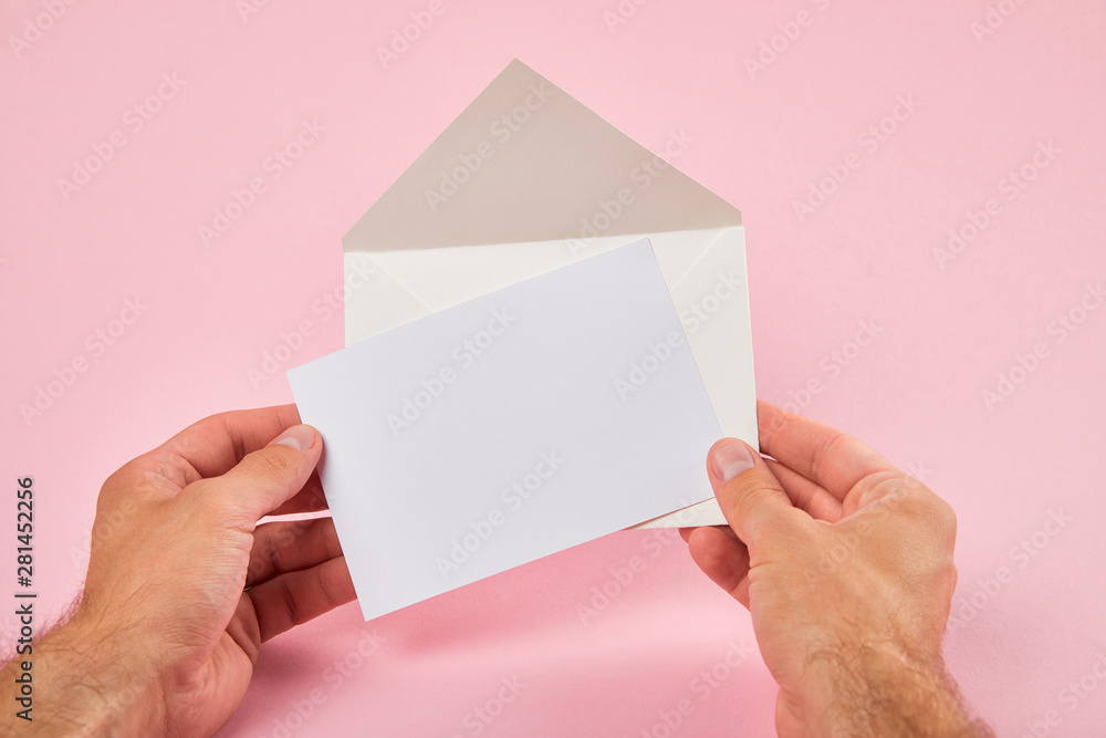 cropped view of man holding envelope and blank white card on pink background