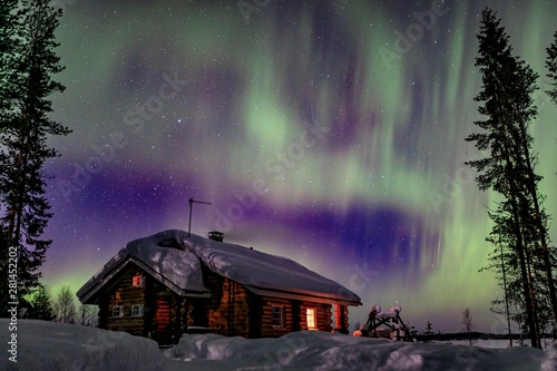 Polar arctic Northern lights Aurora Borealis activity over wooden hoseu in winter Finland, Lapland photo
