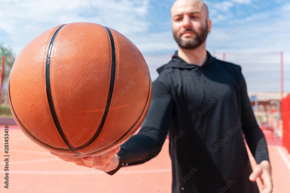 Close up of attractive man holding basket ball. Ball is on focus and foreground.