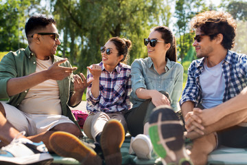 leisure, picnic and people concept - friends hanging out and talking outdoors in summer park