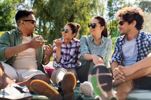 leisure, picnic and people concept - friends hanging out and talking outdoors in summer park