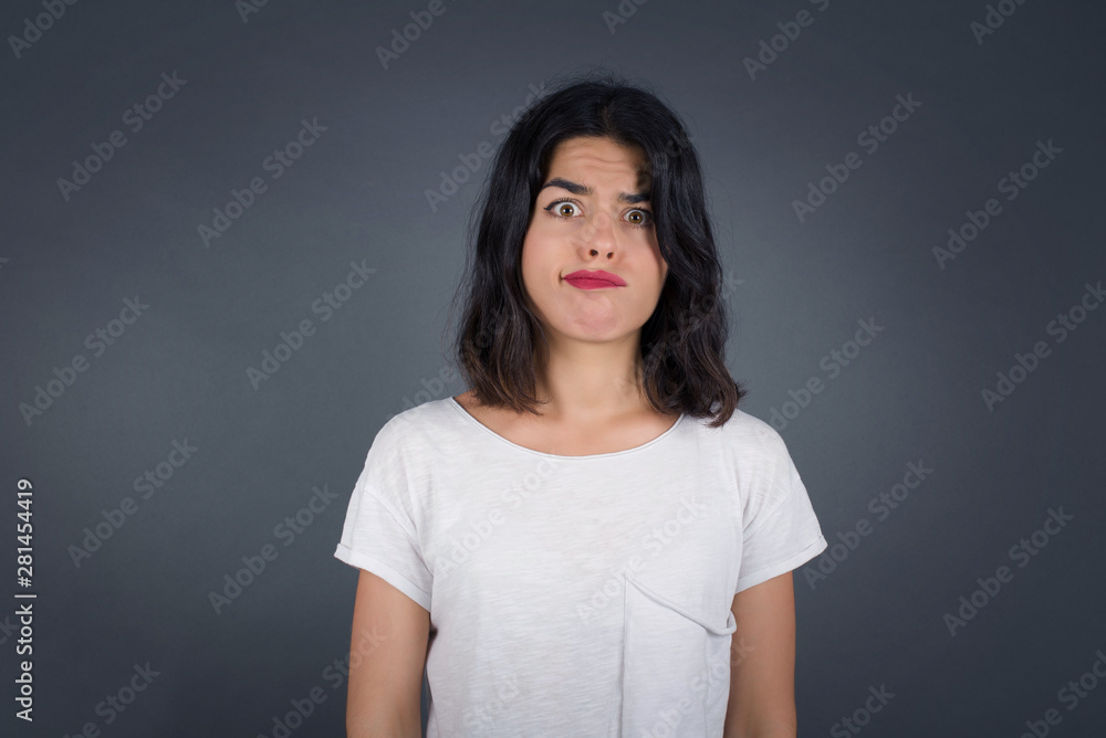 Funny comic girl crosses eyes, puts lips, makes grimace, foolishes after all day studying. Clueless woman nerd with awkward expression has fun alone, plays fool. Wears white sweater Funny comic girl crosses eyes, puts lips, makes grimace, foolishes after all day studying. Clueless woman nerd with awkward expression has fun alone, plays fool. Wears white sweater