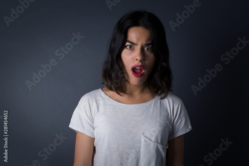 Expressive facial expressions. Shocked stupefied female with red painted lips and make up, keeps jaw dropped, wears striped casual sweater, feels stunned from what she sees aside on blank gray Wall