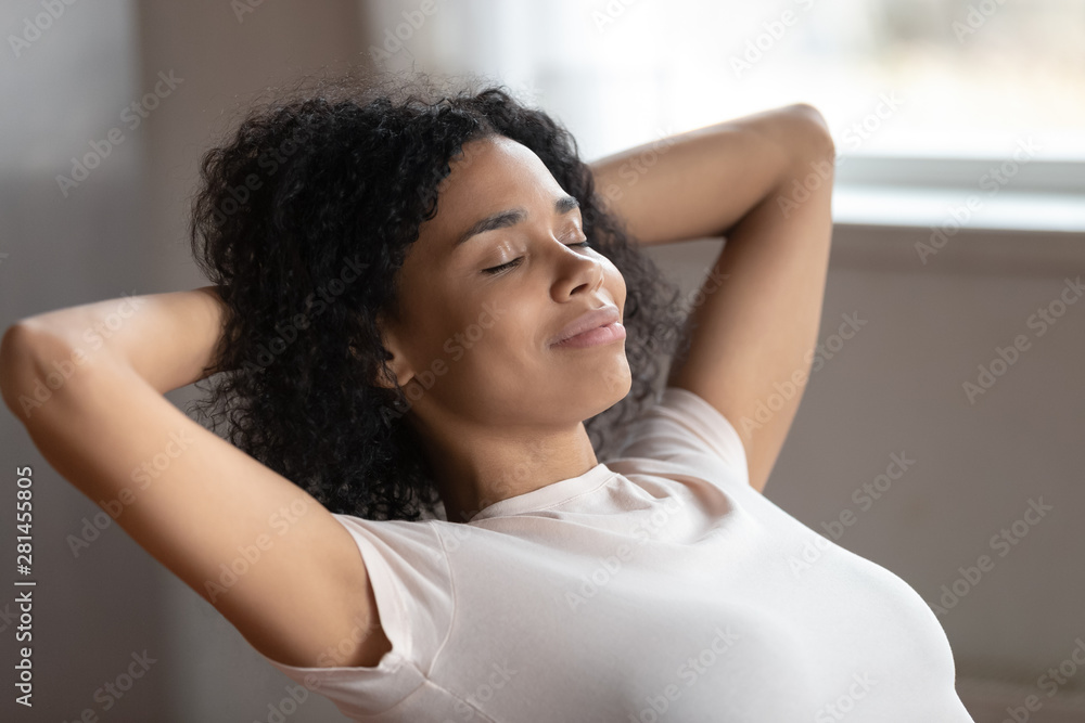 Mixed race woman putting hands behind head resting indoors - obrazy, fototapety, plakaty 