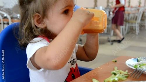 childhood and people concept - little baby drinking from spout cup sitting in highchair at home or at cafe dabbles, disobeys, builds faces, mom tries to feed photo