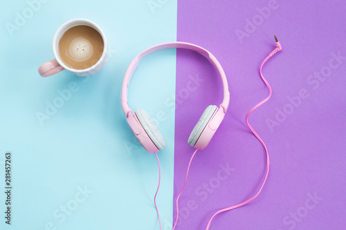 Pink headphones and coffee cup on color background. Music concept