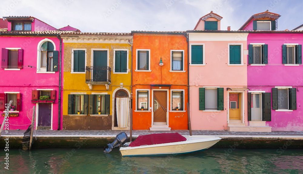 bright colored picturesque buildings near a chanel with boat , houses of Burano in the evening