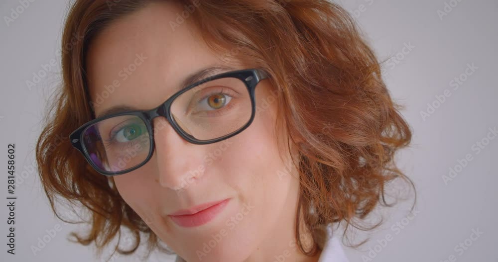 Closeup macro portrait of adult redhead caucasian businesswoman in glasses looking at camera indoors in the white apartment Closeup macro portrait of adult redhead caucasian businesswoman in glasses looking at camera indoors in the white apartment