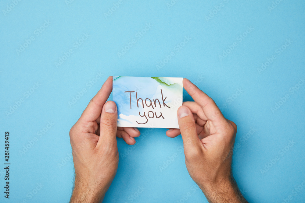partial view of man holding greeting card with thank you lettering on blue background partial view of man holding greeting card with thank you lettering on blue background
