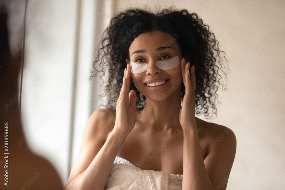 Fototapeta premium Attractive african woman applied under-eye patches looking in mirror