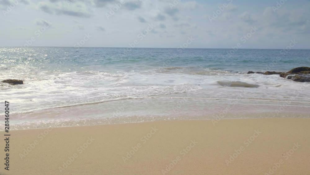A handheld shot of tropical beach with sand and big waves crushing stone with seaweed A handheld shot of tropical beach with sand and big waves crushing stone with seaweed