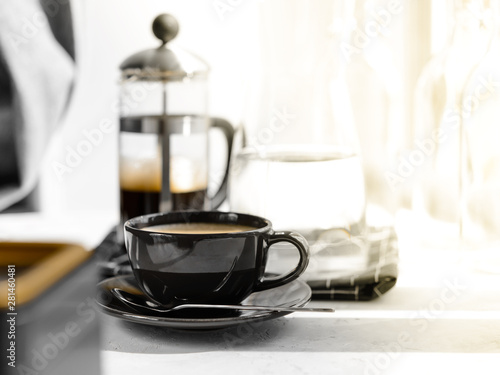 Coffee in black Cup on white background, table. French press,carafe of water, napkin, sunlight. Breakfast.