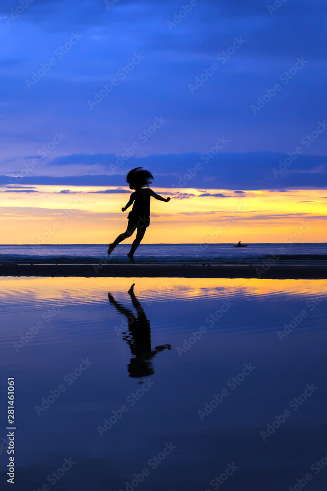 Silhouette of a happy lady jumping on the beach during a beautiful sunrise