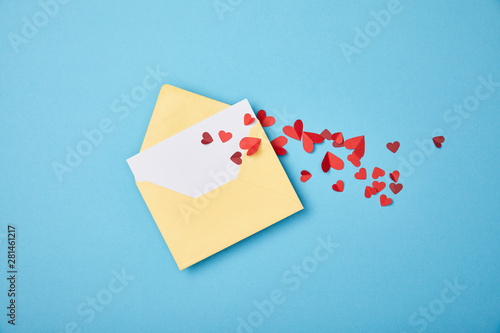 yellow envelope with blank white card and paper cut hearts on blue background