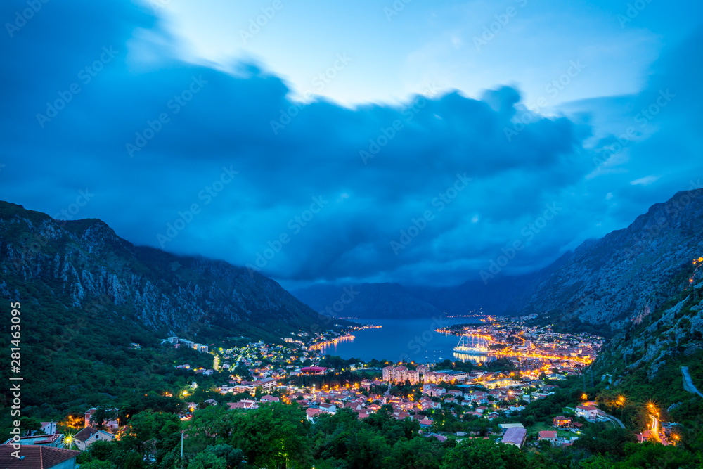 Monenegro, View above houses, streets and port of kotor bay city surrounded by mountains and trees after sunset in twilight atmosphere of illuminated town
