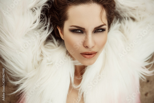 Fashionable and stylish portrait of a beautiful and magnificent young brunette woman with sexy makeup  full lips  smokey eyes  and loose hair in a white gorgeous fur coat