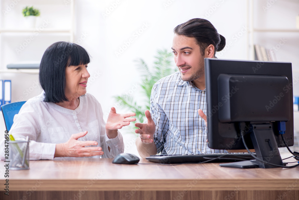 Young male employee explaining to old female colleague how to us Young male employee explaining to old female colleague how to us