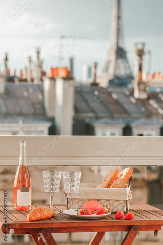 Paris luxury lifestyle. Pink wine, two glasses, traditional french bakery products - baguettes, macaron, croissant and strawberries on a balcony with a view on rooftops