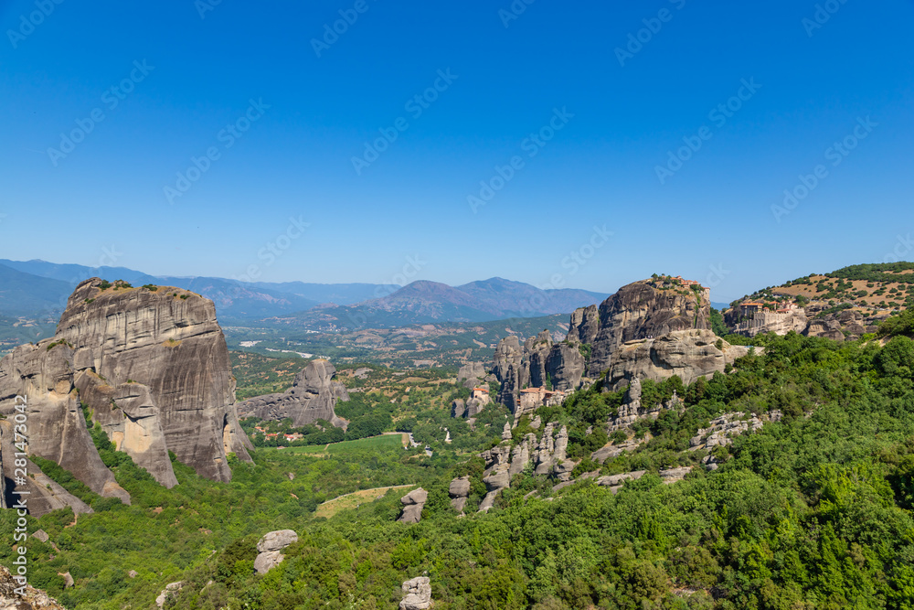 Meteora, Kalmbaka, Greece view overlooking world heritage Greek Orthodox monasteries in a green valley with village and mountains in the background. Breathtaking fairytale valley landscape.