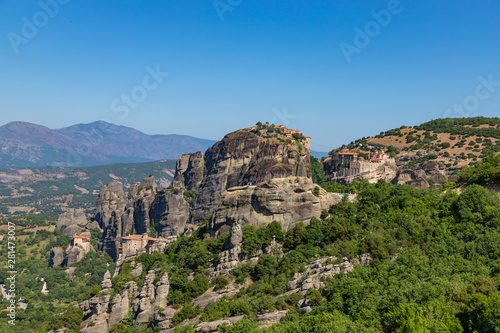 Meteora, Kalmbaka, Greece view overlooking world heritage Greek Orthodox monasteries in a green valley with village and mountains in the background. Breathtaking fairytale valley landscape. © umike_foto