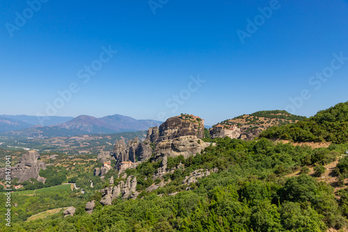 Meteora, Kalmbaka, Greece view overlooking world heritage Greek Orthodox monasteries in a green valley with village and mountains in the background. Breathtaking fairytale valley landscape.