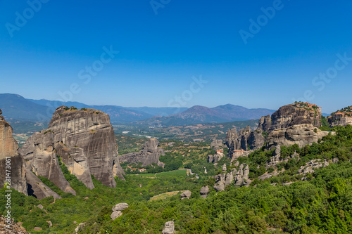 Meteora, Kalmbaka, Greece view overlooking world heritage Greek Orthodox monasteries in a green valley with village and mountains in the background. Breathtaking fairytale valley landscape.