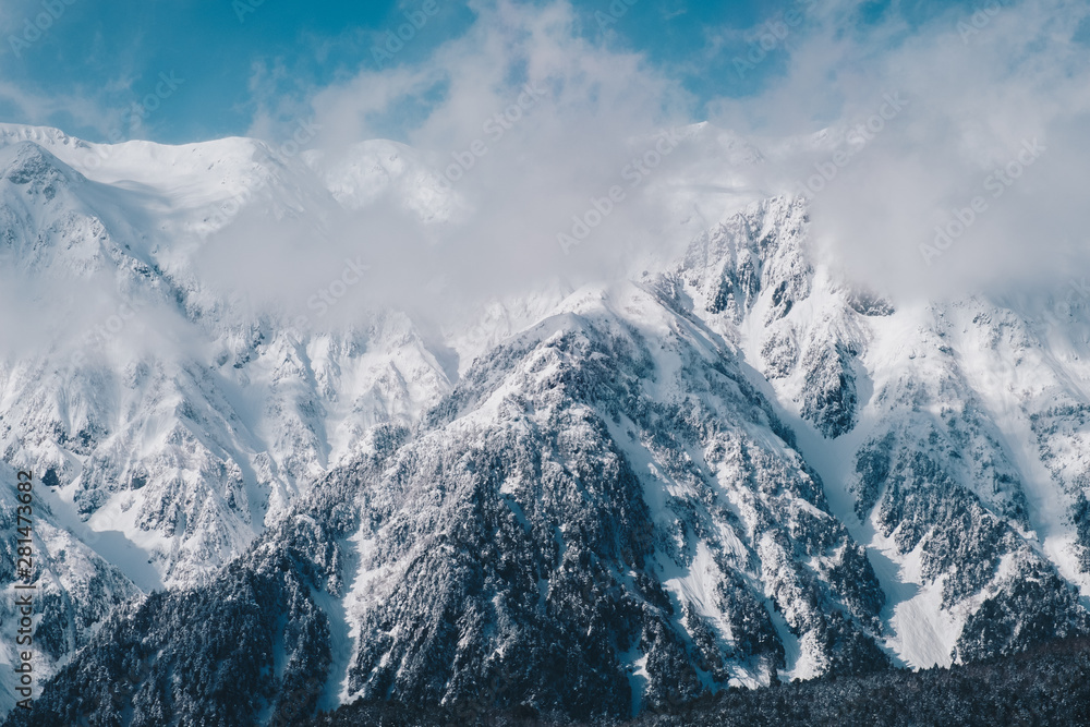 Obraz premium Snow covered pine trees on the background of mountain peaks. Panoramic view of the snowy winter landscape at Shinhotara Ropeway, Japan. Magnificent and silent sunny day.