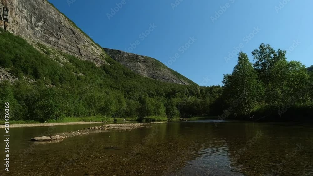 Low angle shot of a peaceful scenery in mountains, from water level of a calm wide rock bottom river surrounded by a forest Low angle shot of a peaceful scenery in mountains, from water level of a calm wide rock bottom river surrounded by a forest