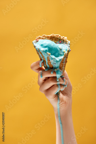 Foto cropped view of woman holding melted blue ice cream in crispy waffle cone isolat