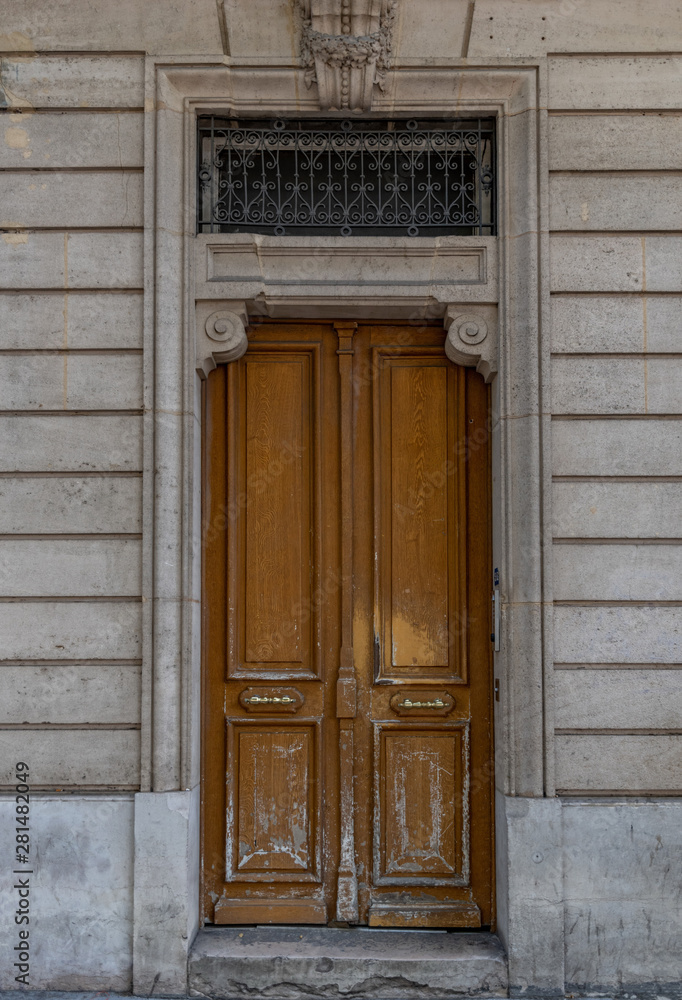Old wooden door in wall. Shabby door entrance of old building in Paris France. Antique wooden doorway and patterned metal grid on window of stone house. Classical style architecture in Europe.