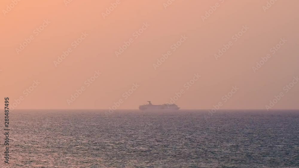 A static time lapse of a cruise ship sailing away in the distance of the Puerto Rican coast at sunset. The orange sun slowly sets on the hazy horizon as the cruise liner passes by the fast waves. A static time lapse of a cruise ship sailing away in the distance of the Puerto Rican coast at sunset. The orange sun slowly sets on the hazy horizon as the cruise liner passes by the fast waves.