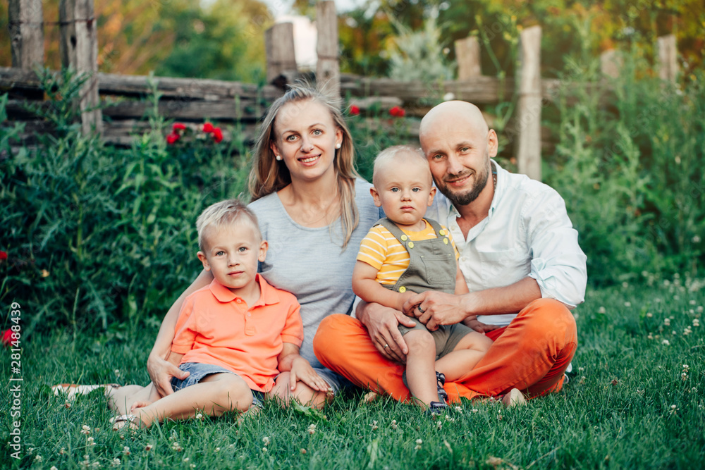 Fototapeta premium Piękny szczęśliwy kaukaski ukraińska rodzina składająca się z czterech osób w parku w letni dzień. Matka i ojciec przytulający rodzeństwo braci dwóch synów. Styl życia autentyczny moment naturalnych emocji.