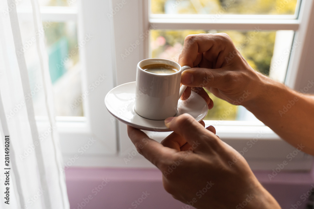 man hands holding small cup of coffee near window in autumn morning