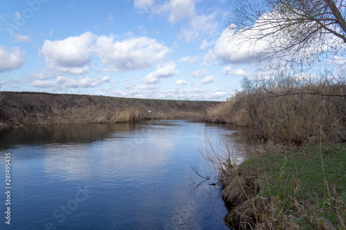 View of the river, shore and blue sky with white cumulus clouds.