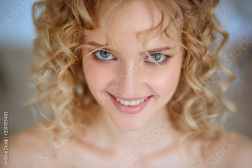 Close up portrait of blonde charming young woman with curly hair and natural makeup. Sunny morning, spa and care