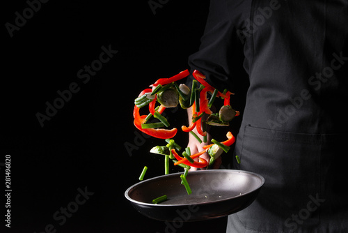 The chef prepares the vegetables in a skillet frying them. Hotel business and the menu in restaurants, the book of recipes. On a black background banner