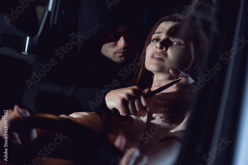 thief strangling beautiful frightened woman in automobile at night with knife photo