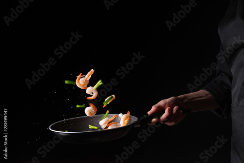 Seafood, chef cooks shrimp with brussels sprouts and pod beans in a frying pan, fry. On a black background for design, menus, restaurants, oriental cuisine, healthy food. Horizontal photo