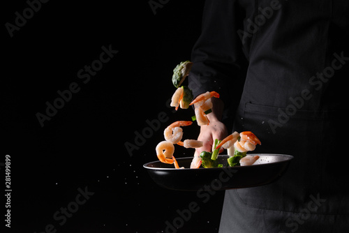 Seafood, chef cooks shrimp with brussels sprouts and pod beans in a frying pan, fry. On a black background for design, menus, restaurants, oriental cuisine, healthy food. Horizontal photo, banner