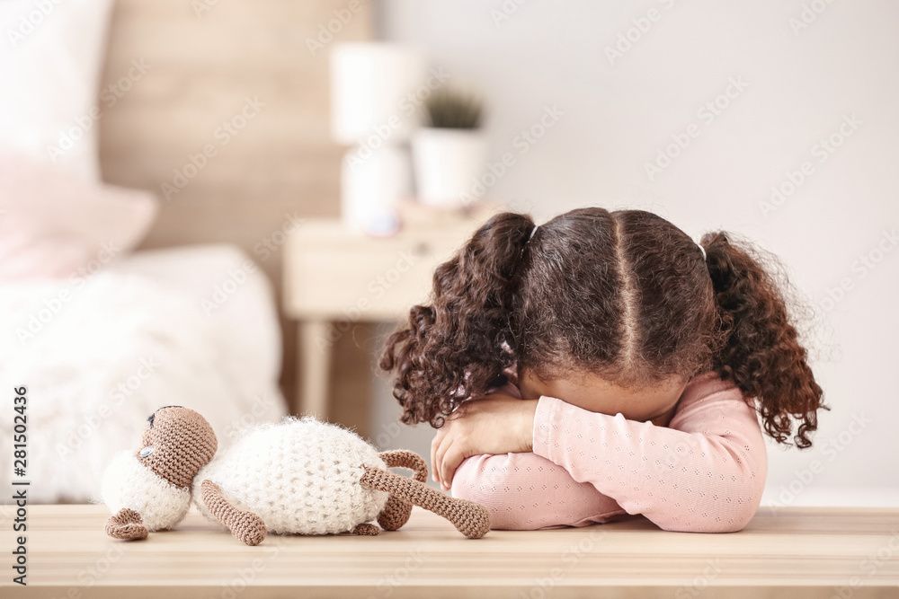 Sad little African-American girl sitting at table - obrazy, fototapety, plakaty 