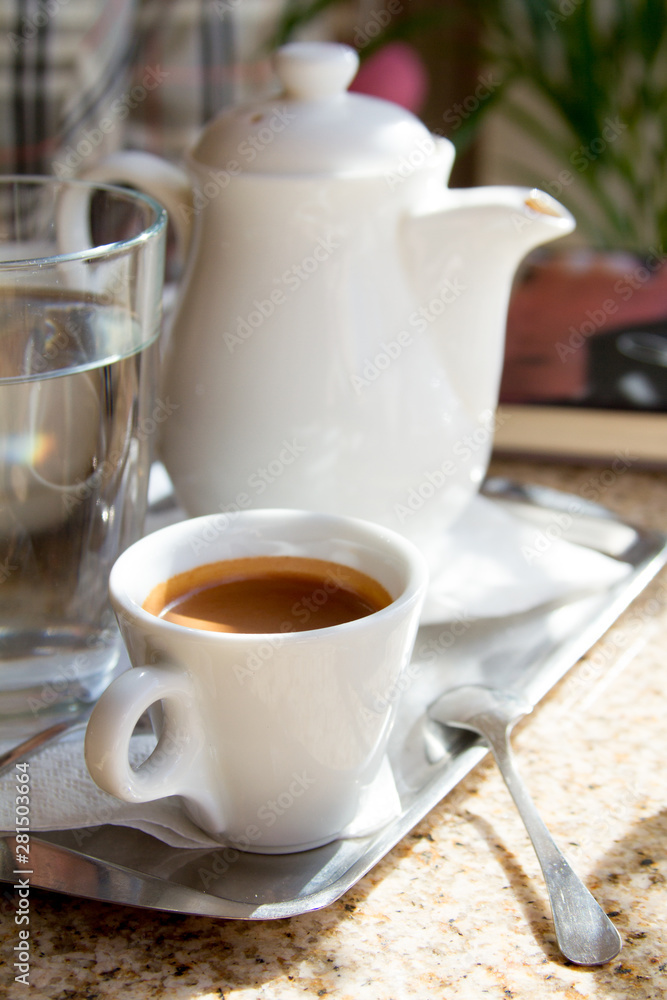 Close-up on a tray white porcelain coffee pot and a cup with freshly brewed espresso on the terrace, selective focus Close-up on a tray white porcelain coffee pot and a cup with freshly brewed espresso on the terrace, selective focus